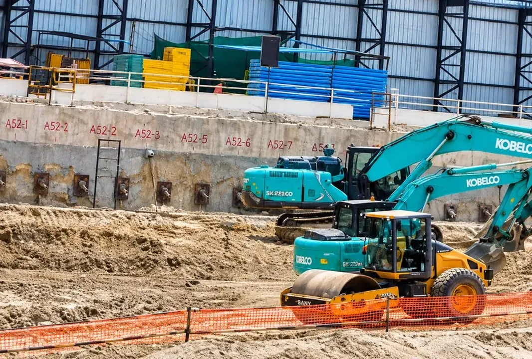Excavators and a roller working inside a basement pit with an anchored retaining wall